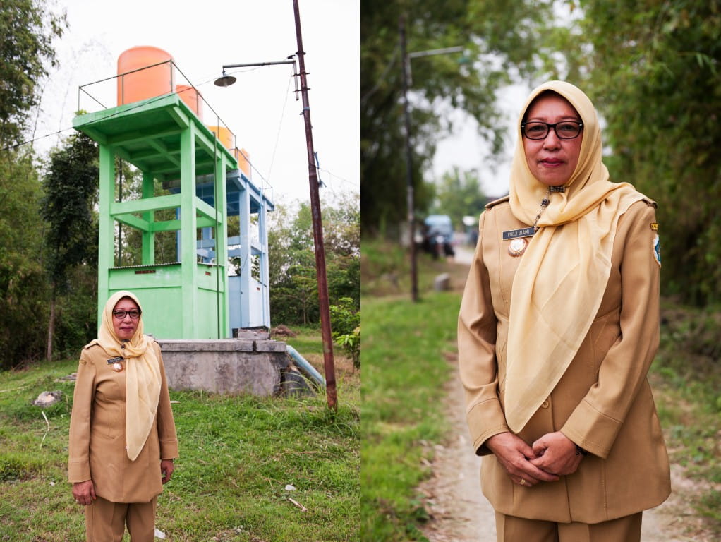 Village head Ibu Puji Utami stands in front of water storage tanks built by the local water association that supply the village with water. However, the water distributed to homes is not treated for direct consumption, posing some health risks.