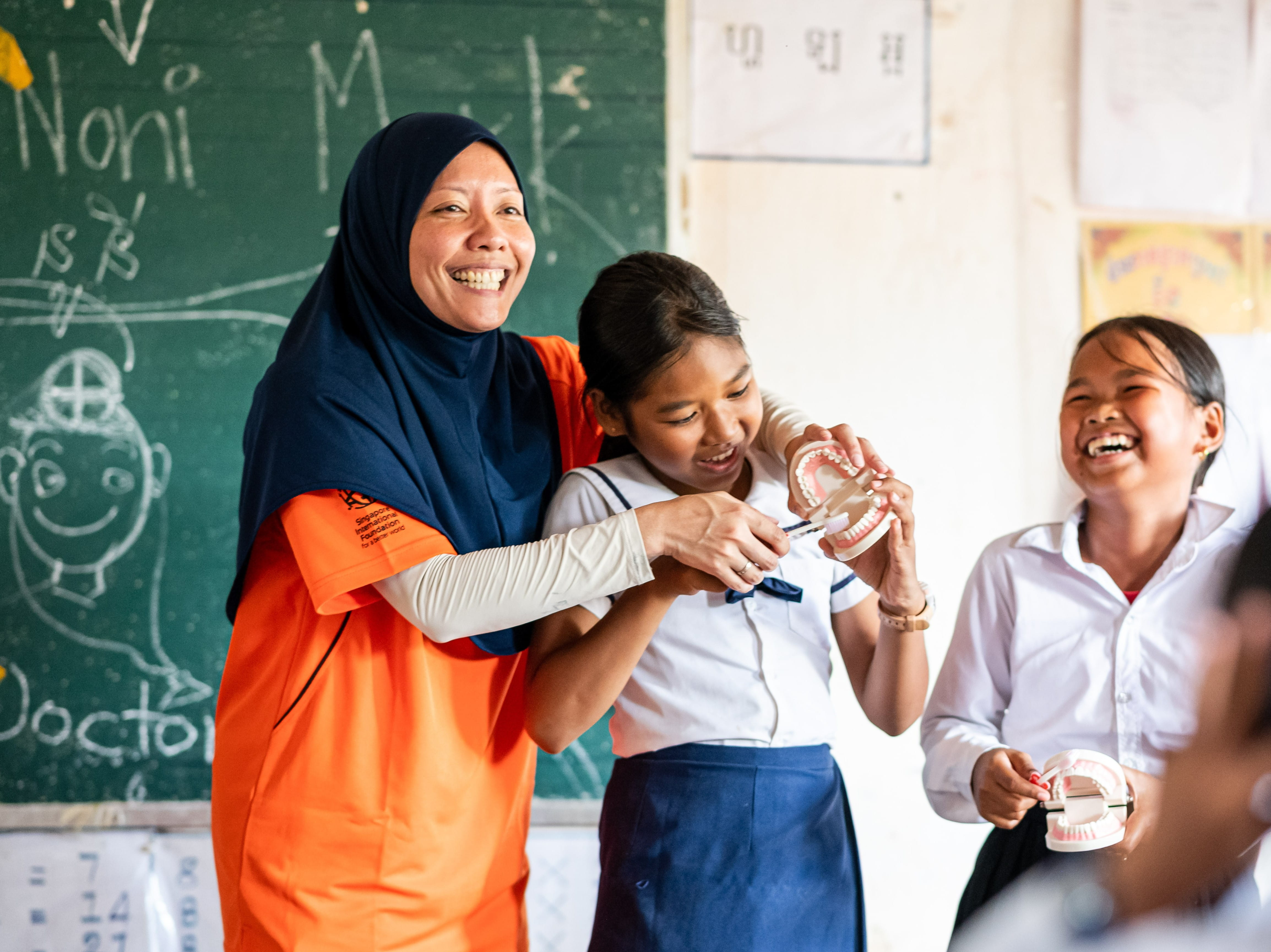 Singapore International Volunteer (SIV) Azlina Ahmad (in orange) showing Cambodian students how to brush properly to care for the teeth and gums, as part of basic hygiene training for schoolchildren. Hygiene education is one of the two parts of the WFL programme, with the other part being the installation of bio-sand water filters.