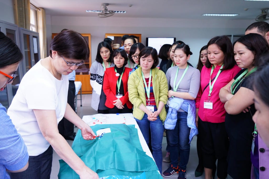 Ms Chan Siew Mie (left, in white top), Singapore International Volunteer and Senior Nurse Manager from Tan Tock Seng Hospital, demonstrating permanent catheter dressing techniques to Vietnamese master trainers during the clinical training workshop.